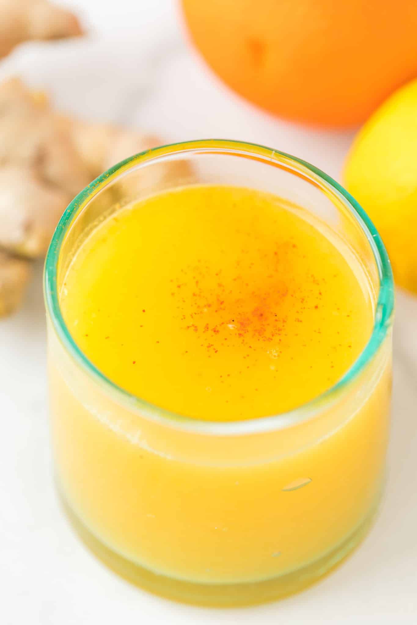 orange ginger lemon juice shot in a pretty glass with cayenne pepper sprinkled on top.