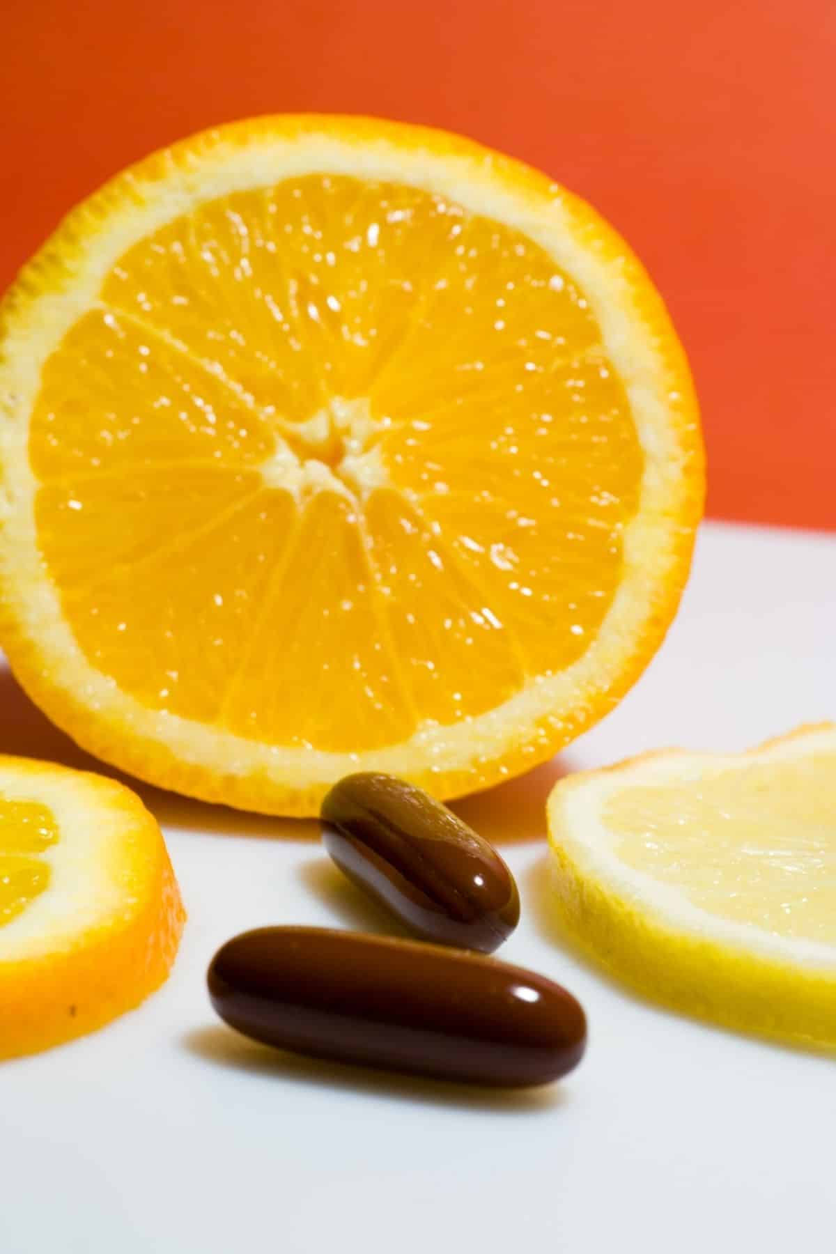 vitamin c capsules in front of a sliced orange.