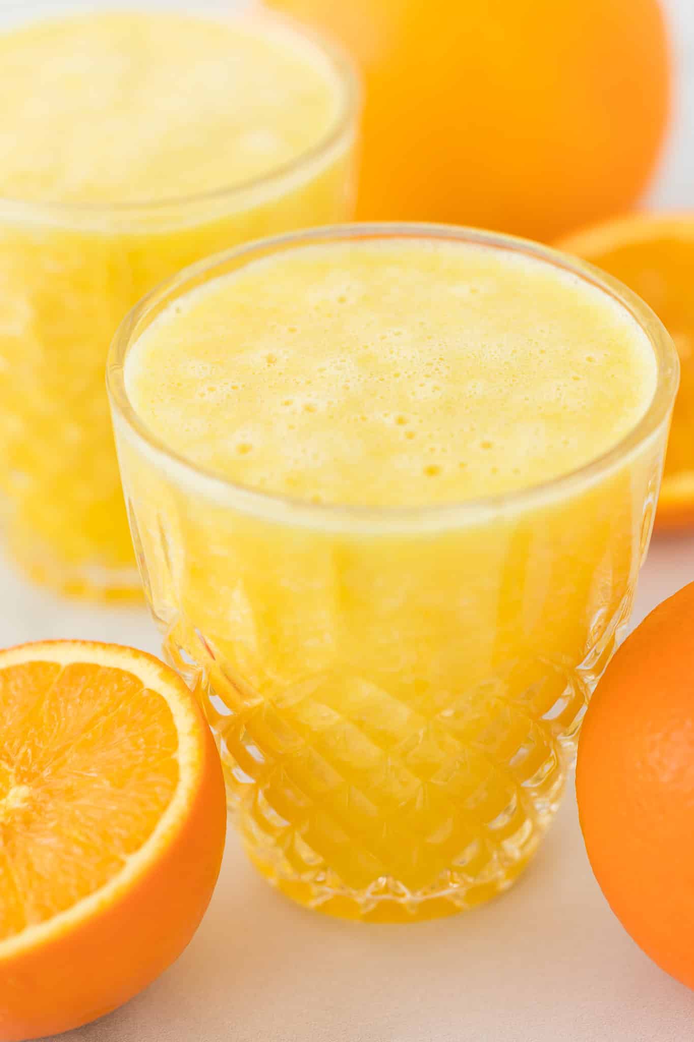 blended orange juice served in a pretty crystal glass surrounded by oranges