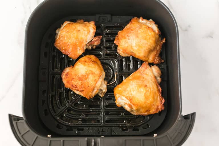 four cooked chicken thighs in the basket of an air fryer