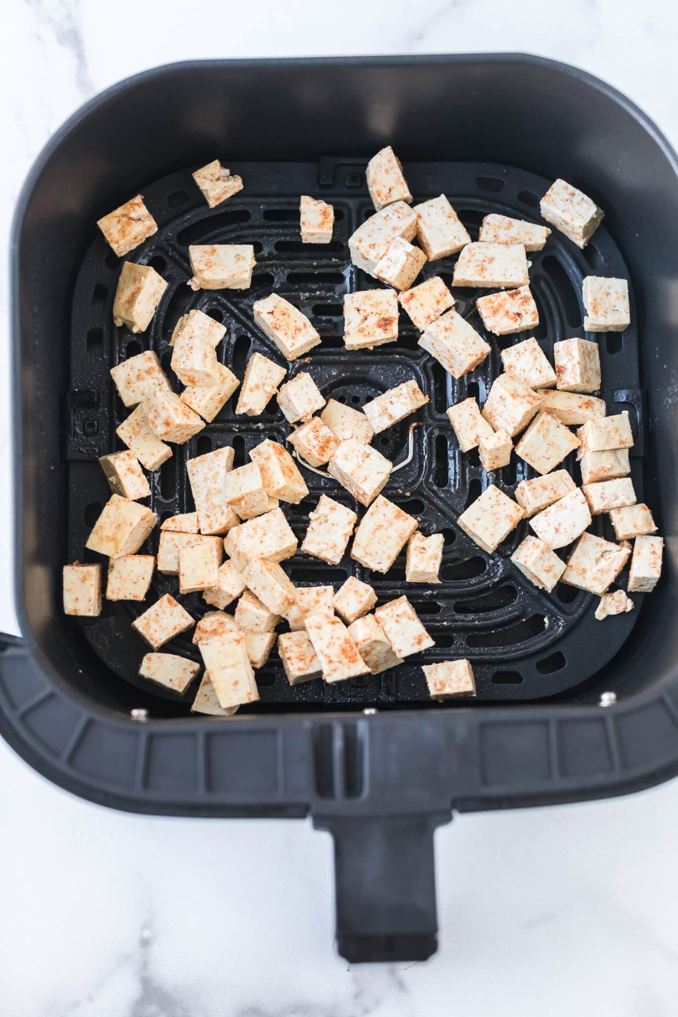 seasoned tofu in the basket of an air fryer ready to be baked