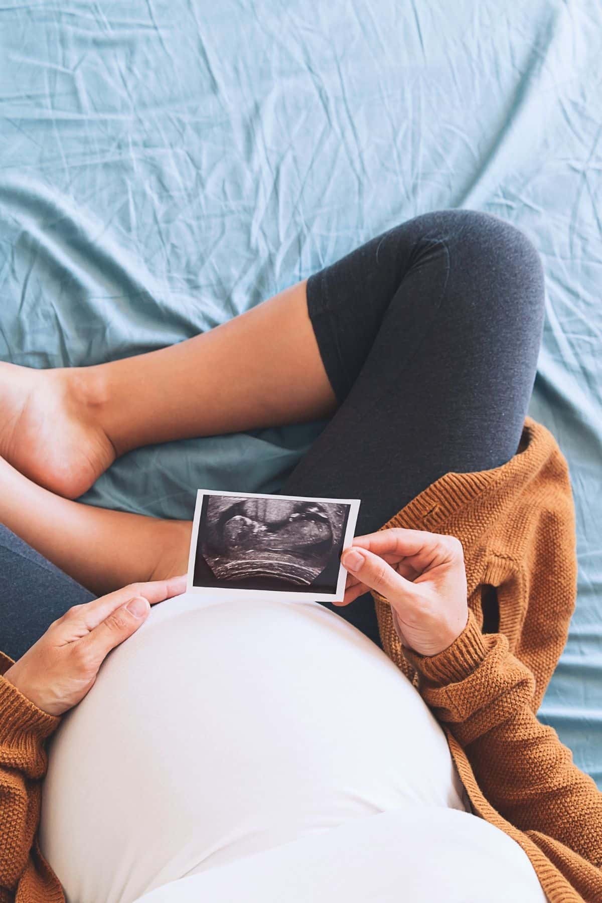 pregnant woman sitting on a bed holding an ultrasound photo.