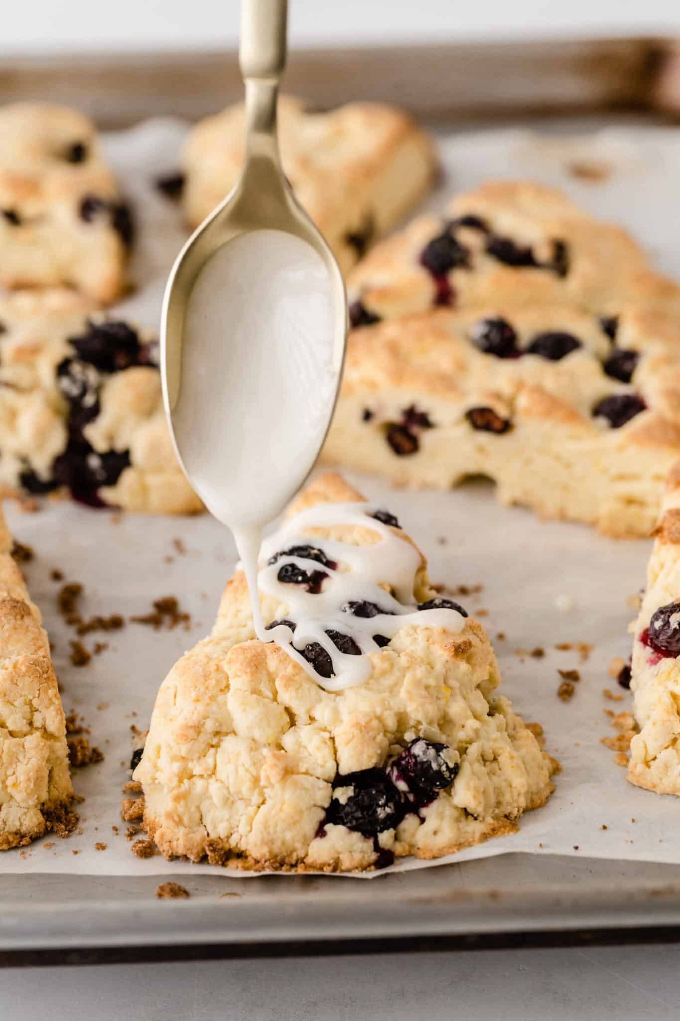 spoon drizzling glaze onto baked gluten free blueberry scones.