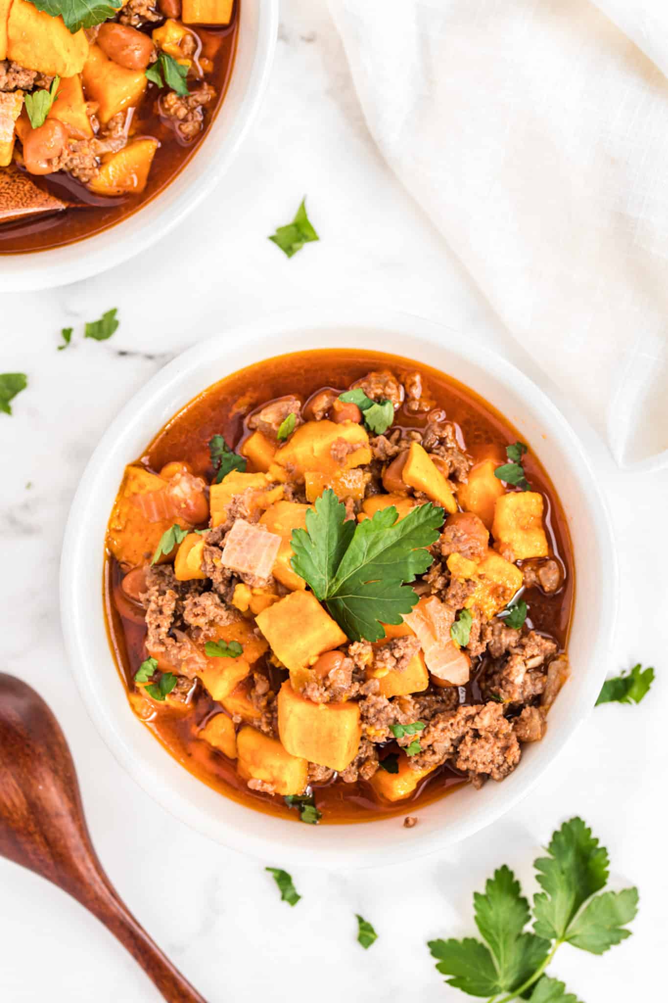 two bowls of sweet potato beef chili with fresh parsley on top.