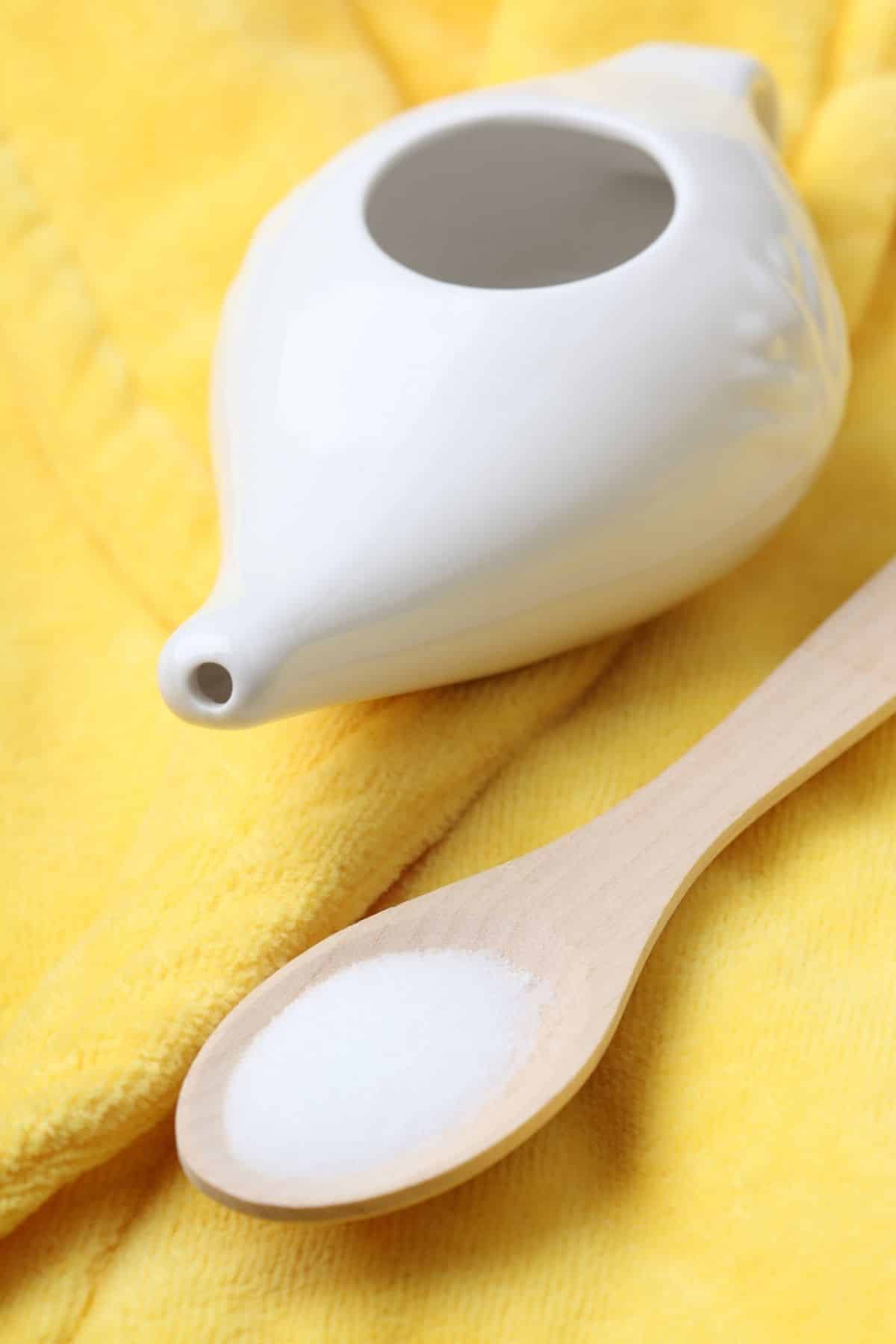 neti pot on a table with a spoonful of salt.