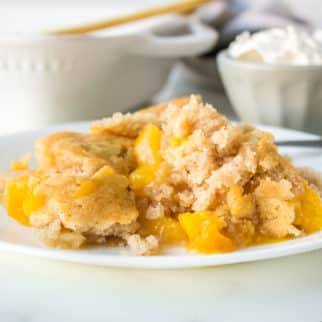 A close up of a plate of cobbler with whipped cream behind it.