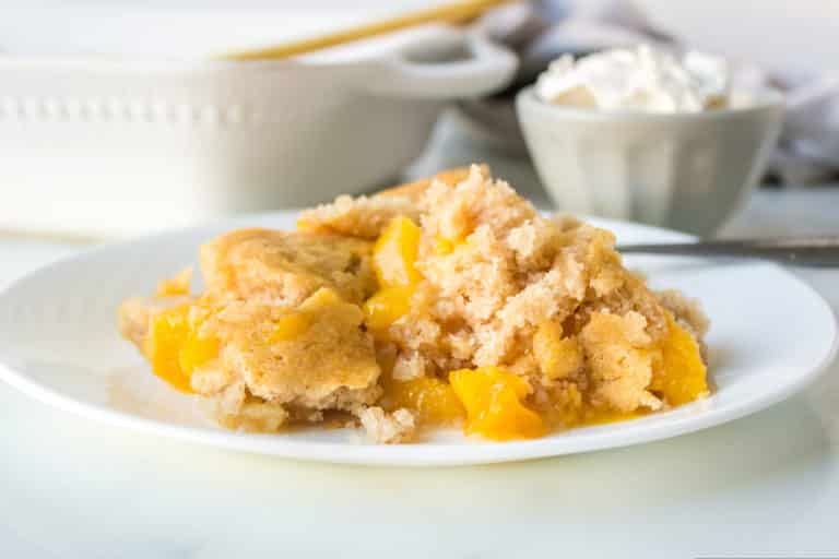 A plate of peach cobbler with a bowl of whipped cream behind it.