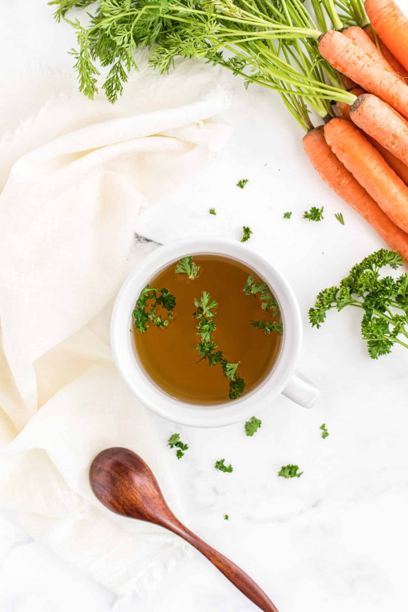 bowl of vegetable broth on a table with fresh carrots.