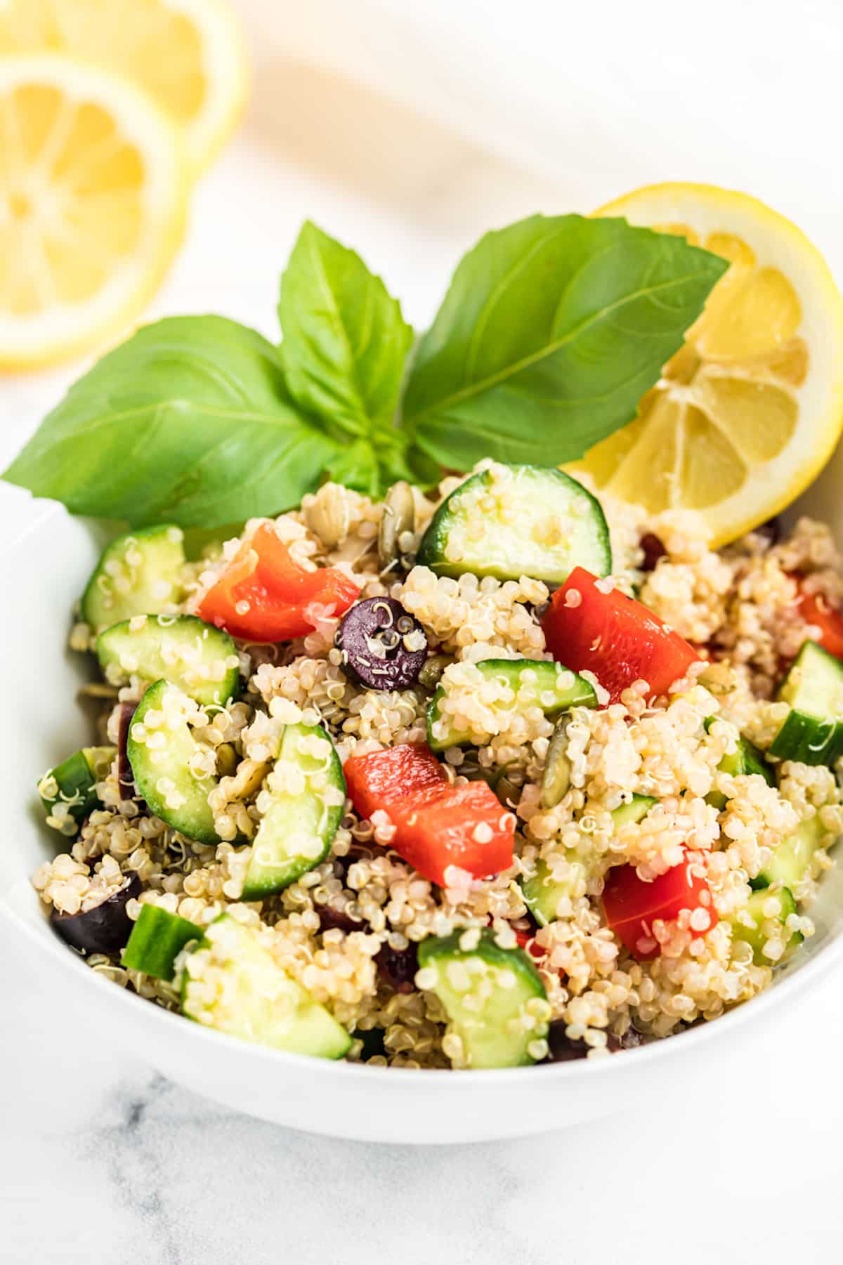 A bowl of quinoa salad with cucumbers, red pepper, and olives