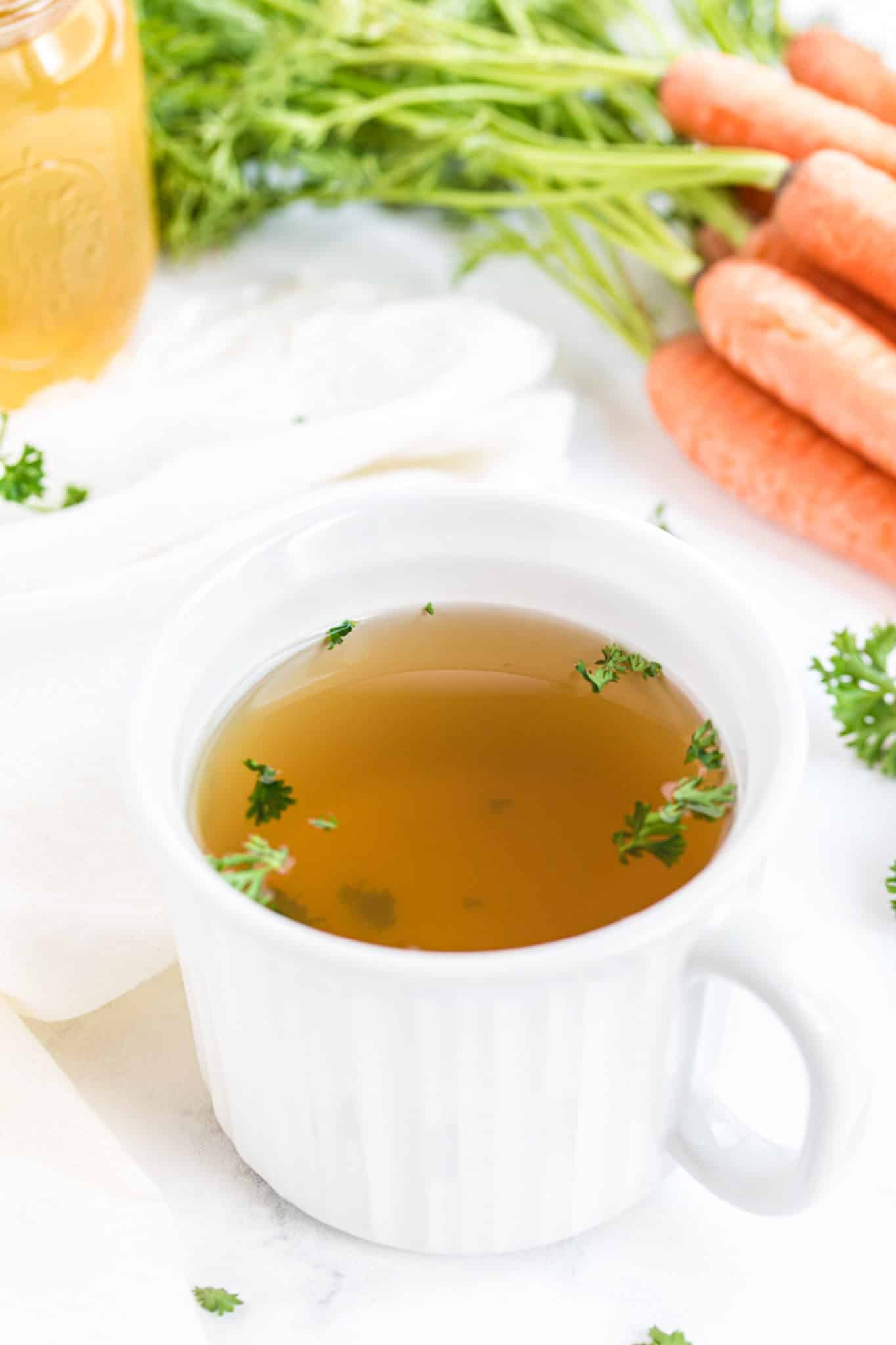 mug of instant pot veggie broth on a table with carrots.
