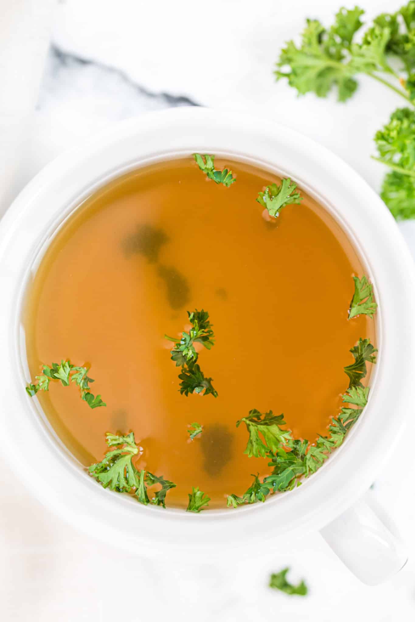 mug of instant pot vegetable broth with fresh parsley on top.
