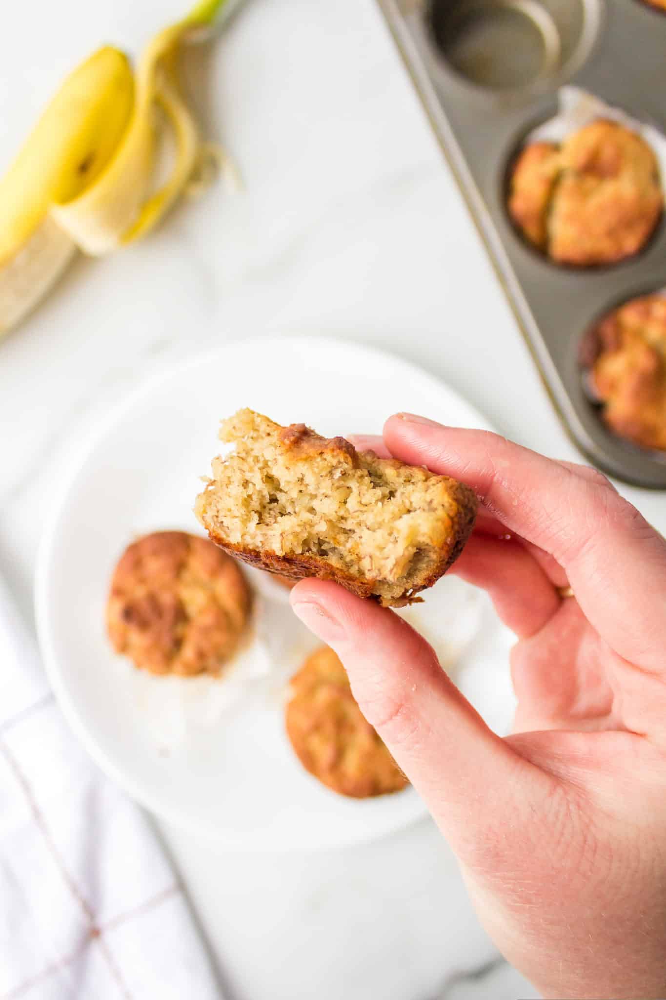 picture of a hand holding a banana almond flour muffin with a bite taken out of it.