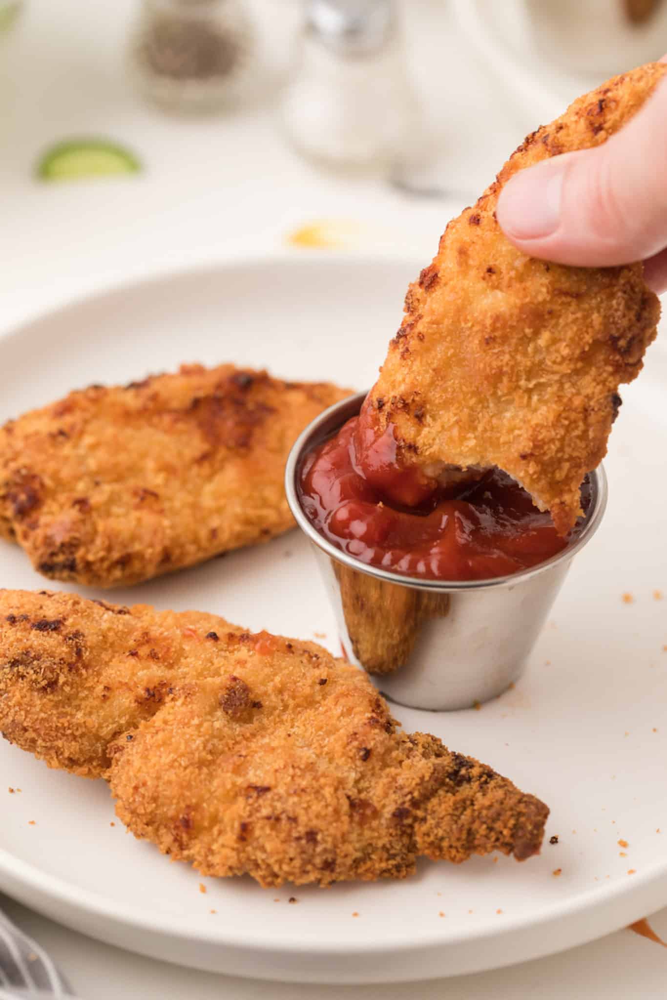 Dipping an air fryer chicken finger in ketchup.