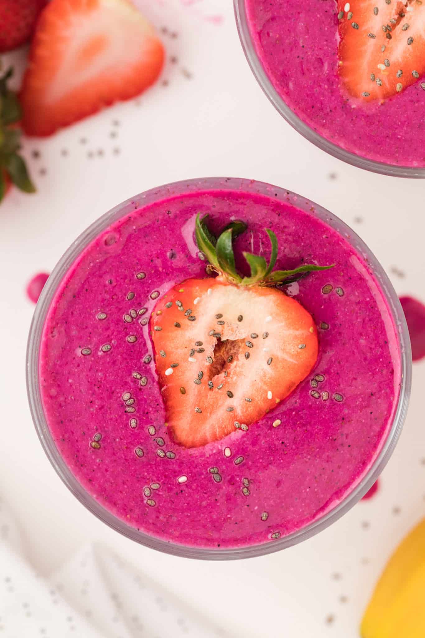 bright pink acai smoothie served in glasses with sliced strawberries