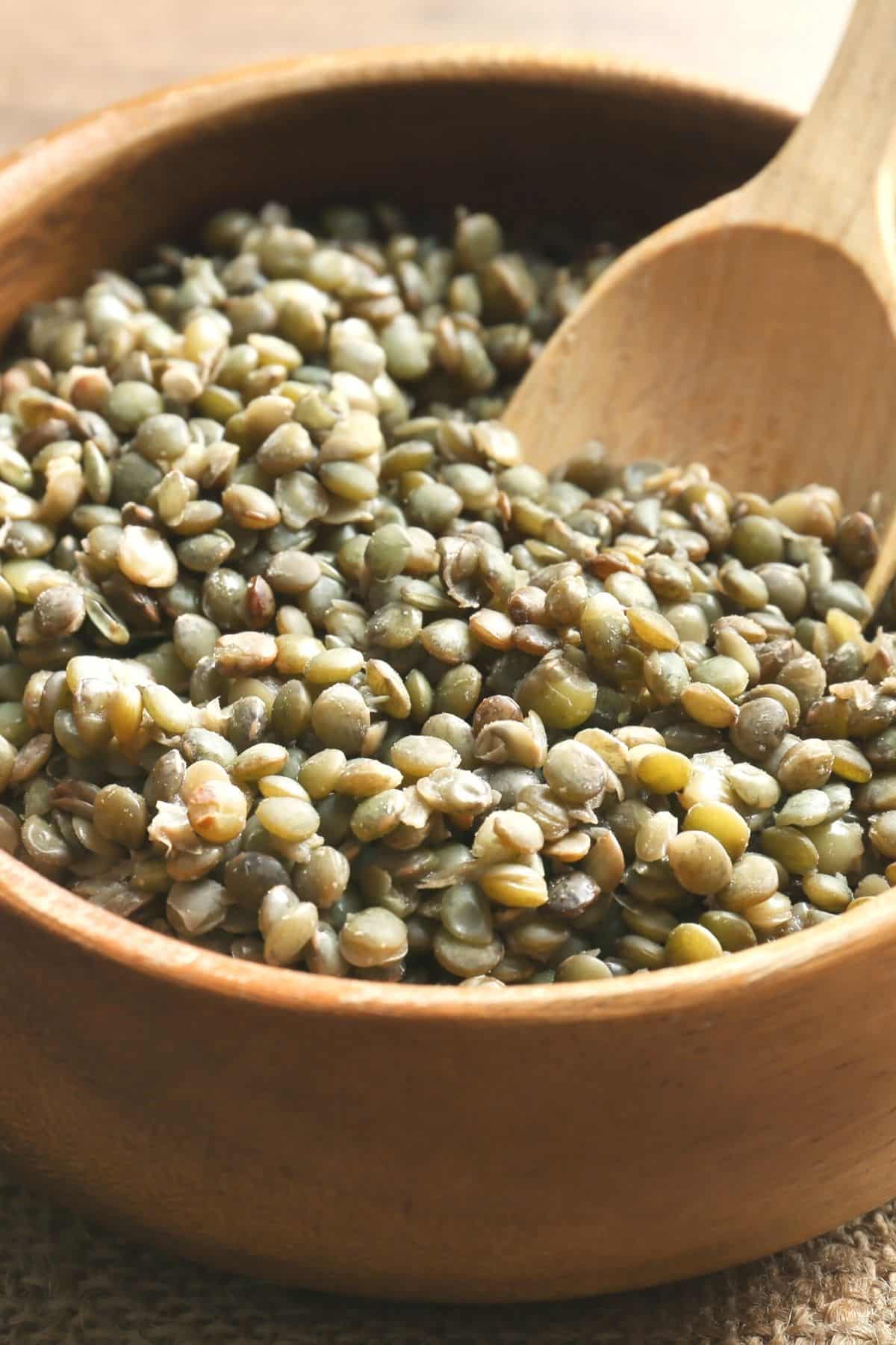 bowl of cooked brown lentils with wooden spoon.