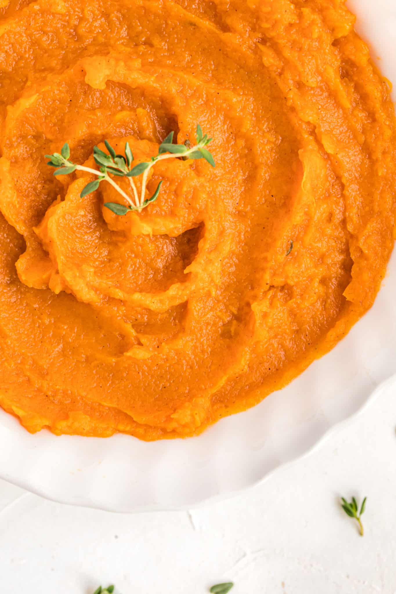 close up of mashed sweet potatoes in a bowl with thyme on top.