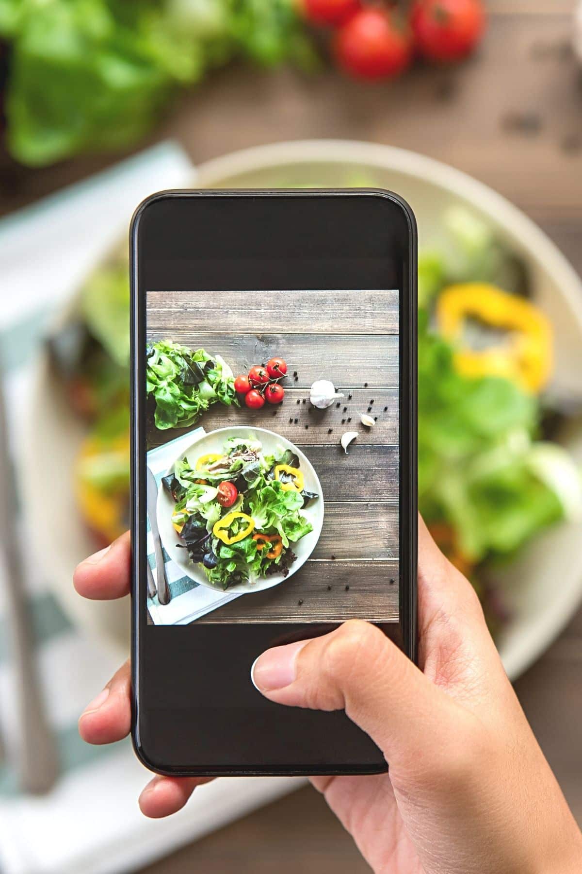 A person taking a picture of a salad with a phone.