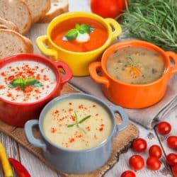 collection of vegetable soups on a tabletop with bread.