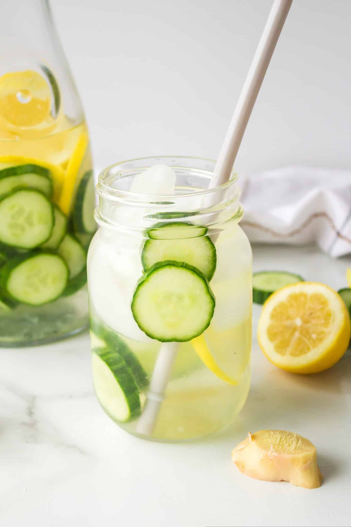 cucumber ginger lemon water in jar with ice cubes and paper straw.