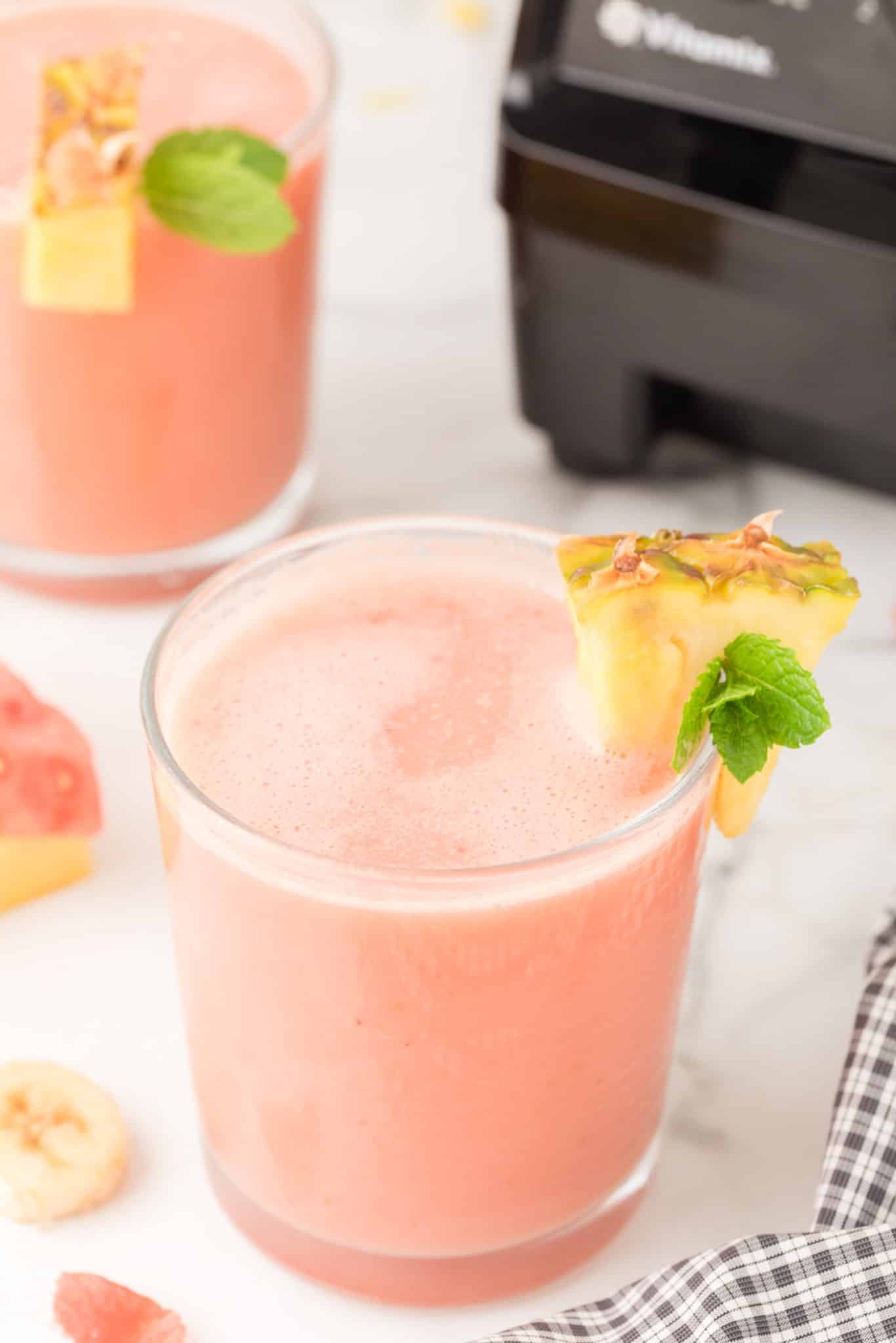 two glasses of watermelon smoothie with pineapple on edge.