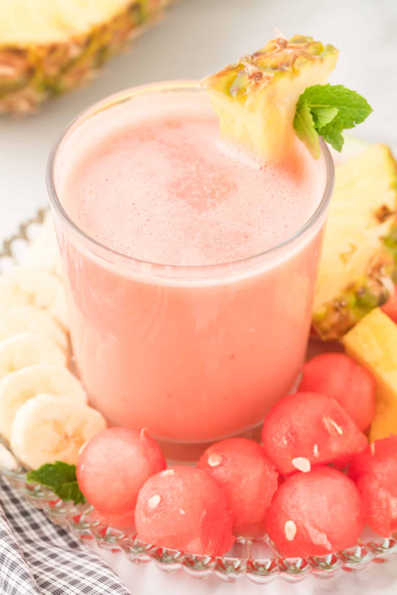 watermelon banana smoothie in a glass with a plate of fresh fruit.