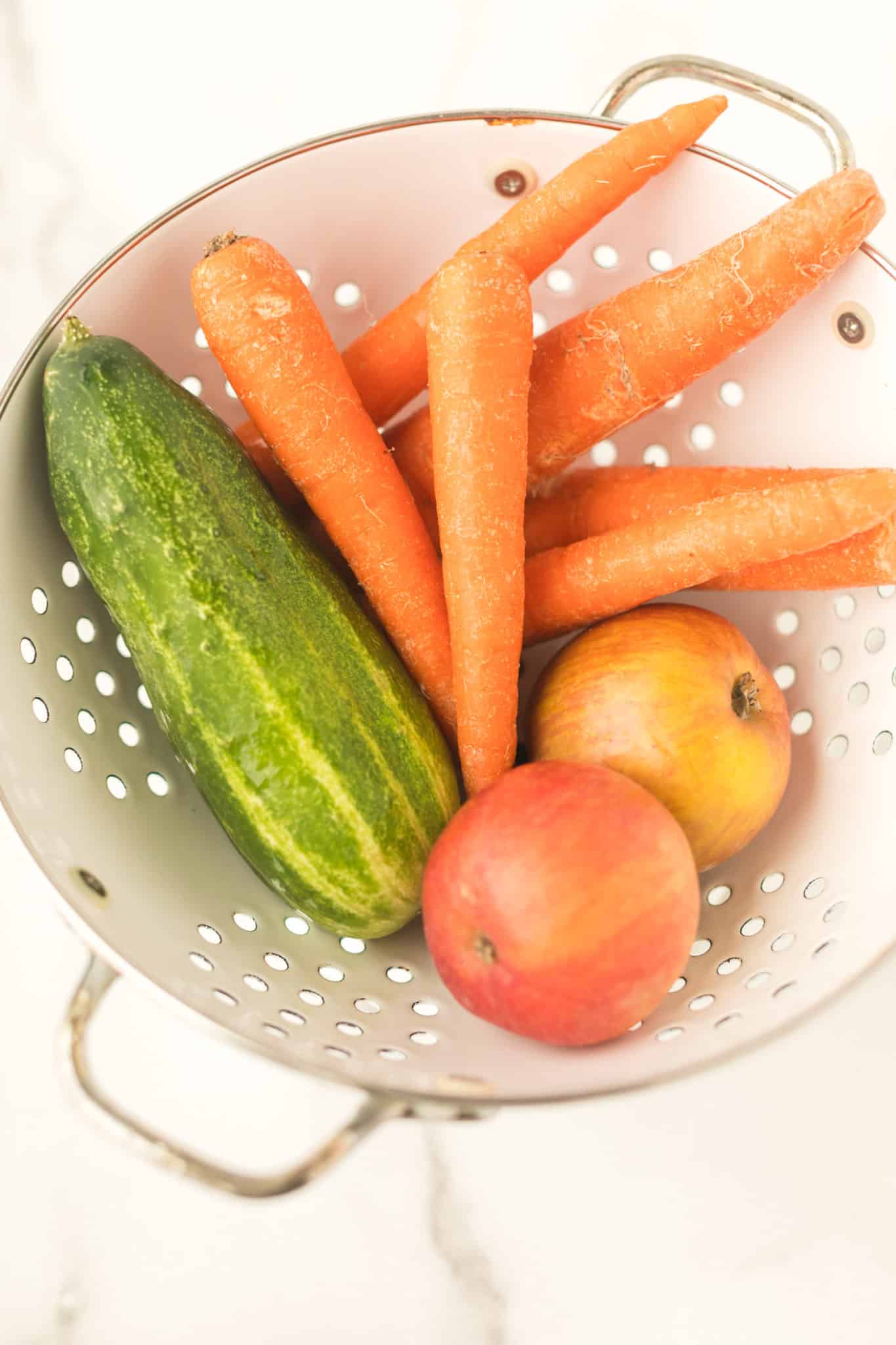 carrots, cucumber, and apple in a colander ready to be juiced.