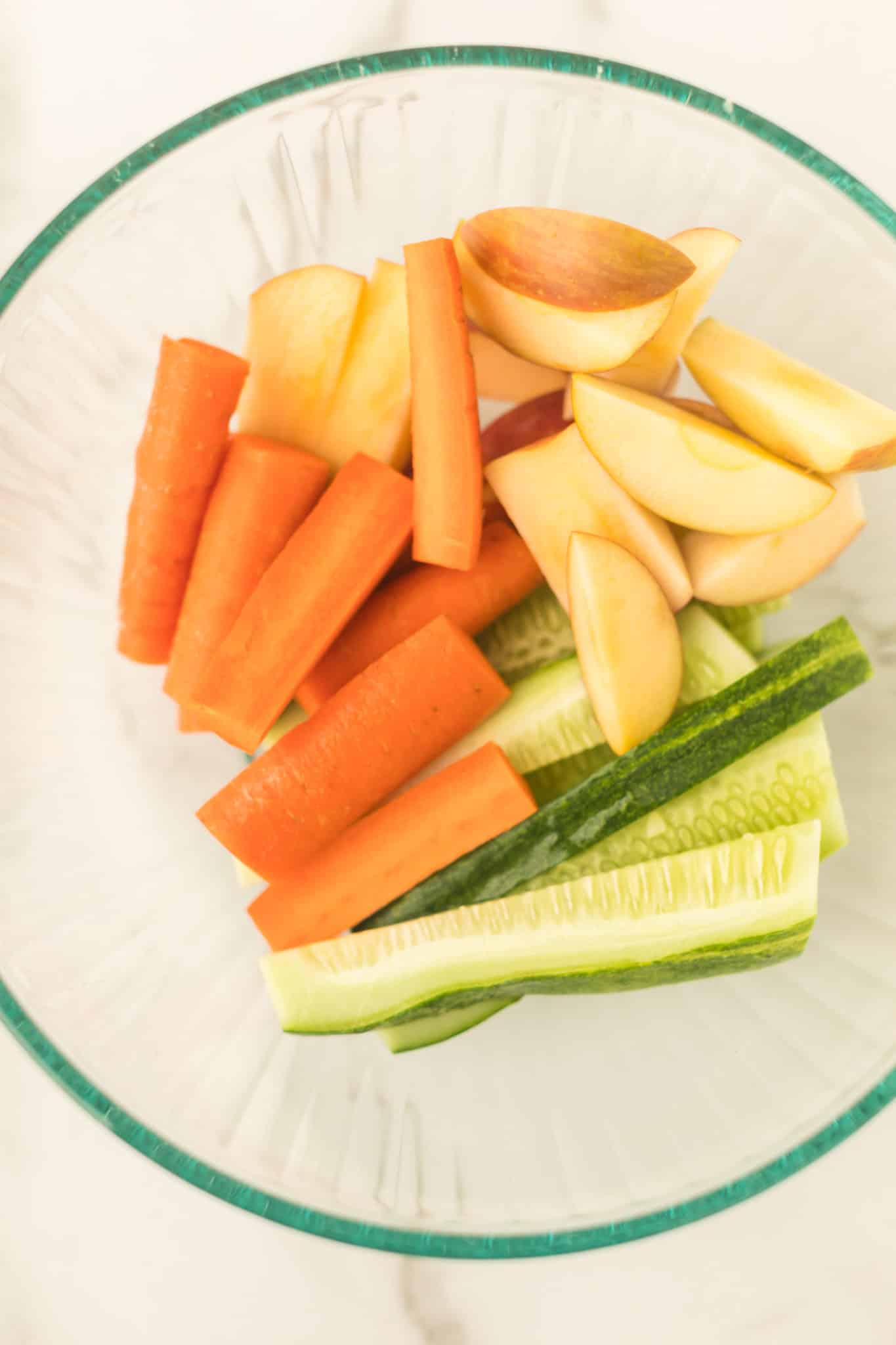 cut up apples, carrots, and cucumber in a bowl.