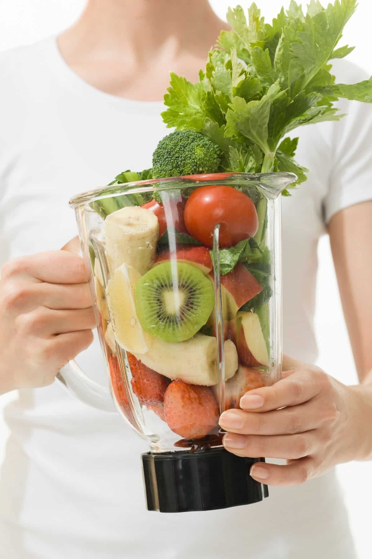 woman holding a blender with fruits and veggies in it.