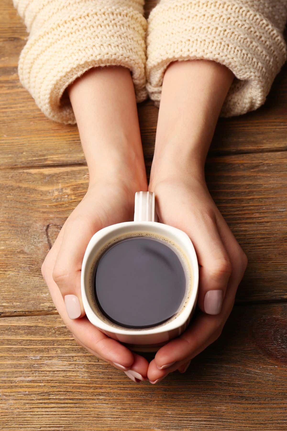 woman holding a mug of organic coffee in her hands on a tabletop.