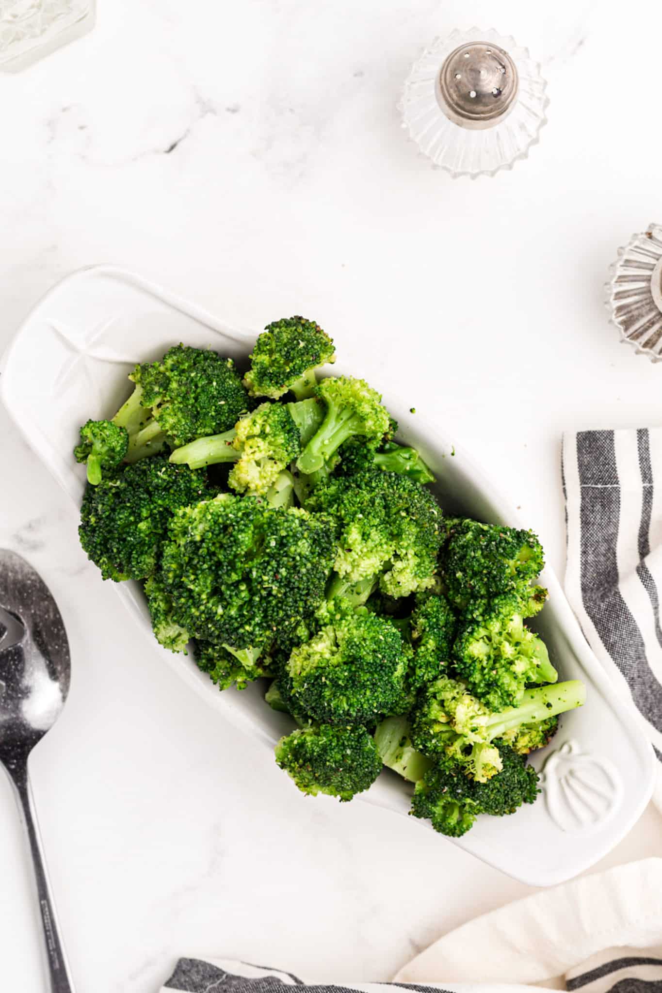 cooked broccoli on a table with salt and pepper shakers