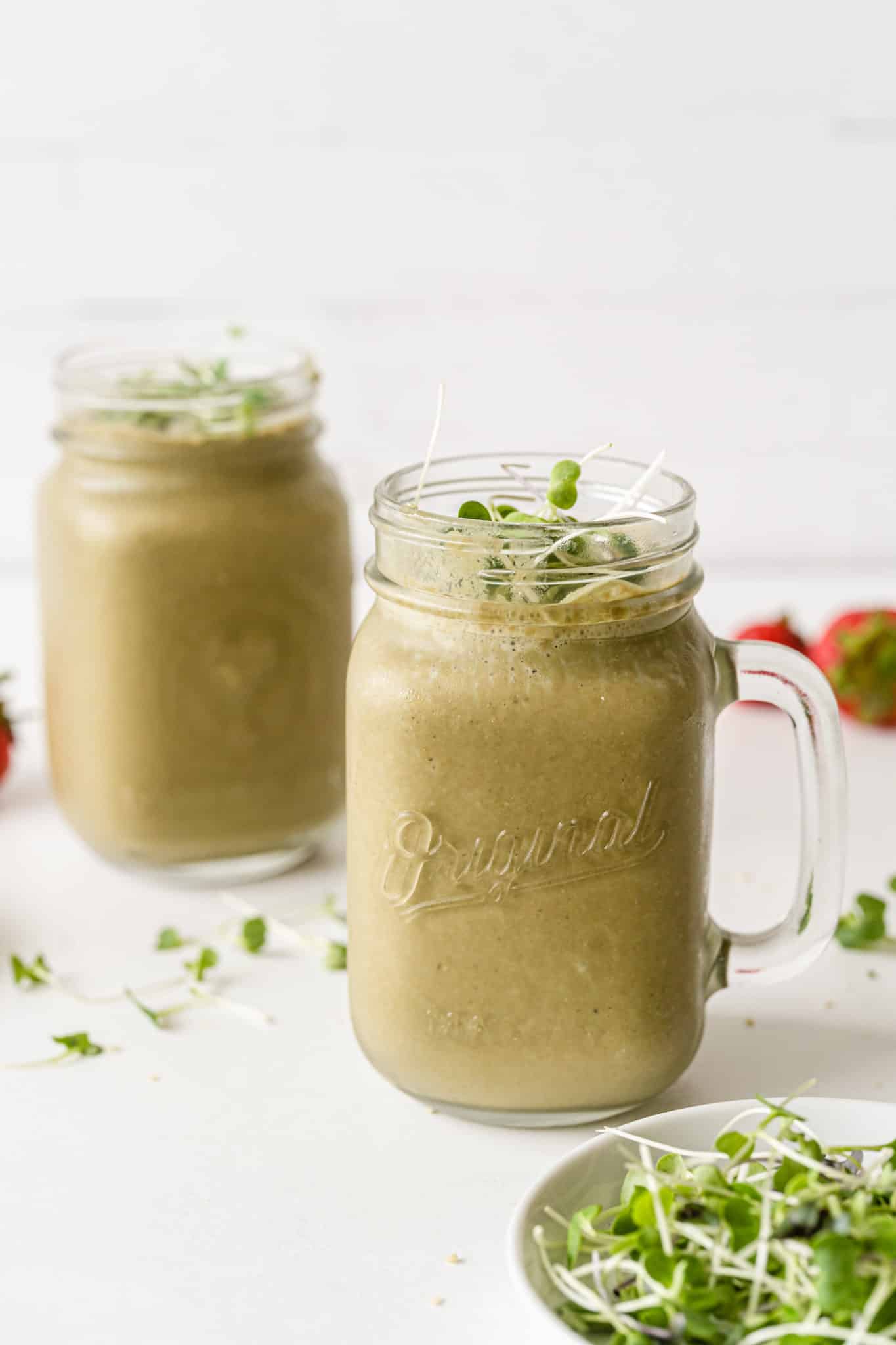 two jars of broccoli sprout smoothie on a table.