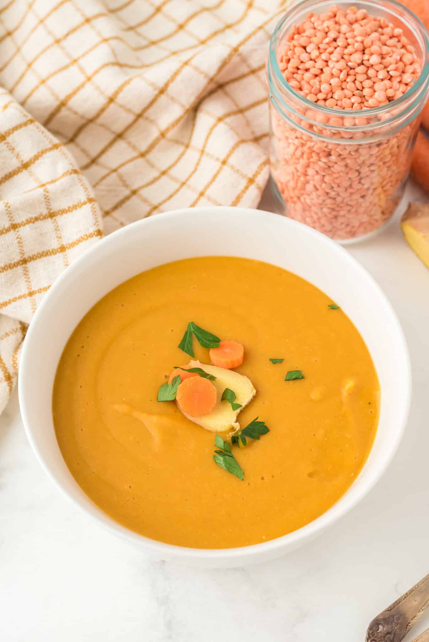 carrot ginger lentil soup served in white bowl.
