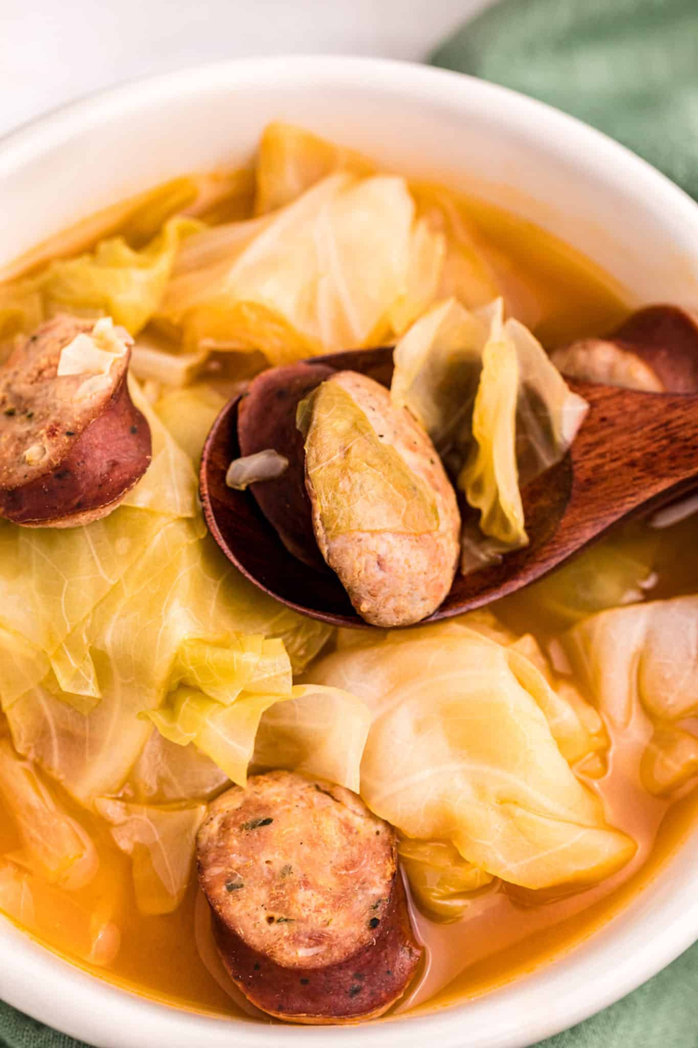 a close up of sausage and cabbage in a bowl with wooden spoon.