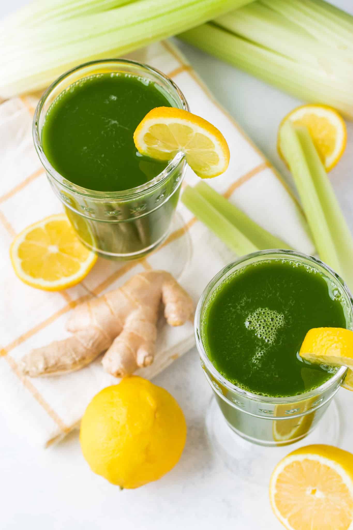 two glasses of green juice with lemon and celery sticks