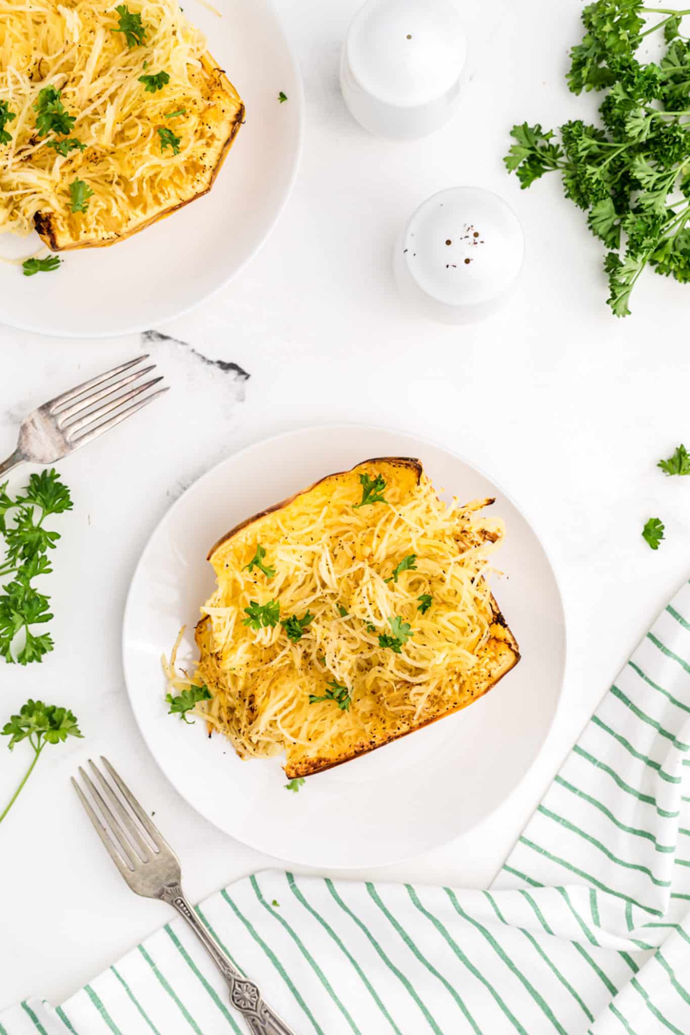 two plates of cooked spaghetti squash with parsley garnish.