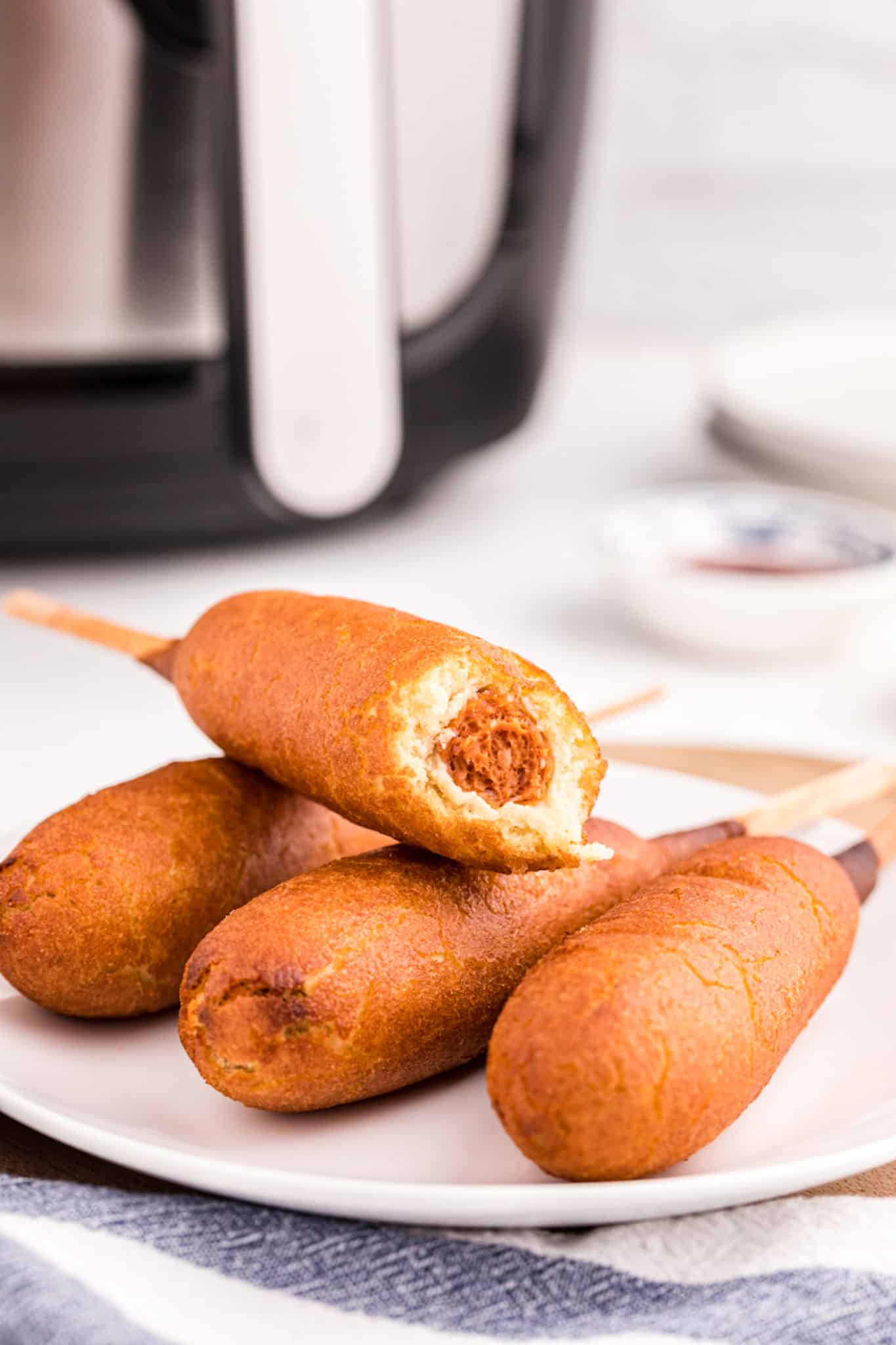 corn dogs on a plate with a bite taken out of one.