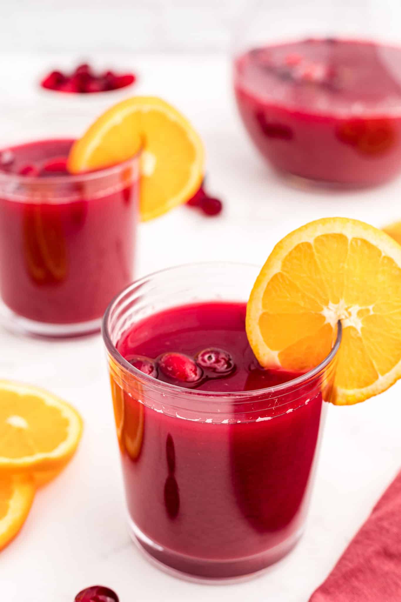 a glass of red holiday brunch punch with a slice of orange.