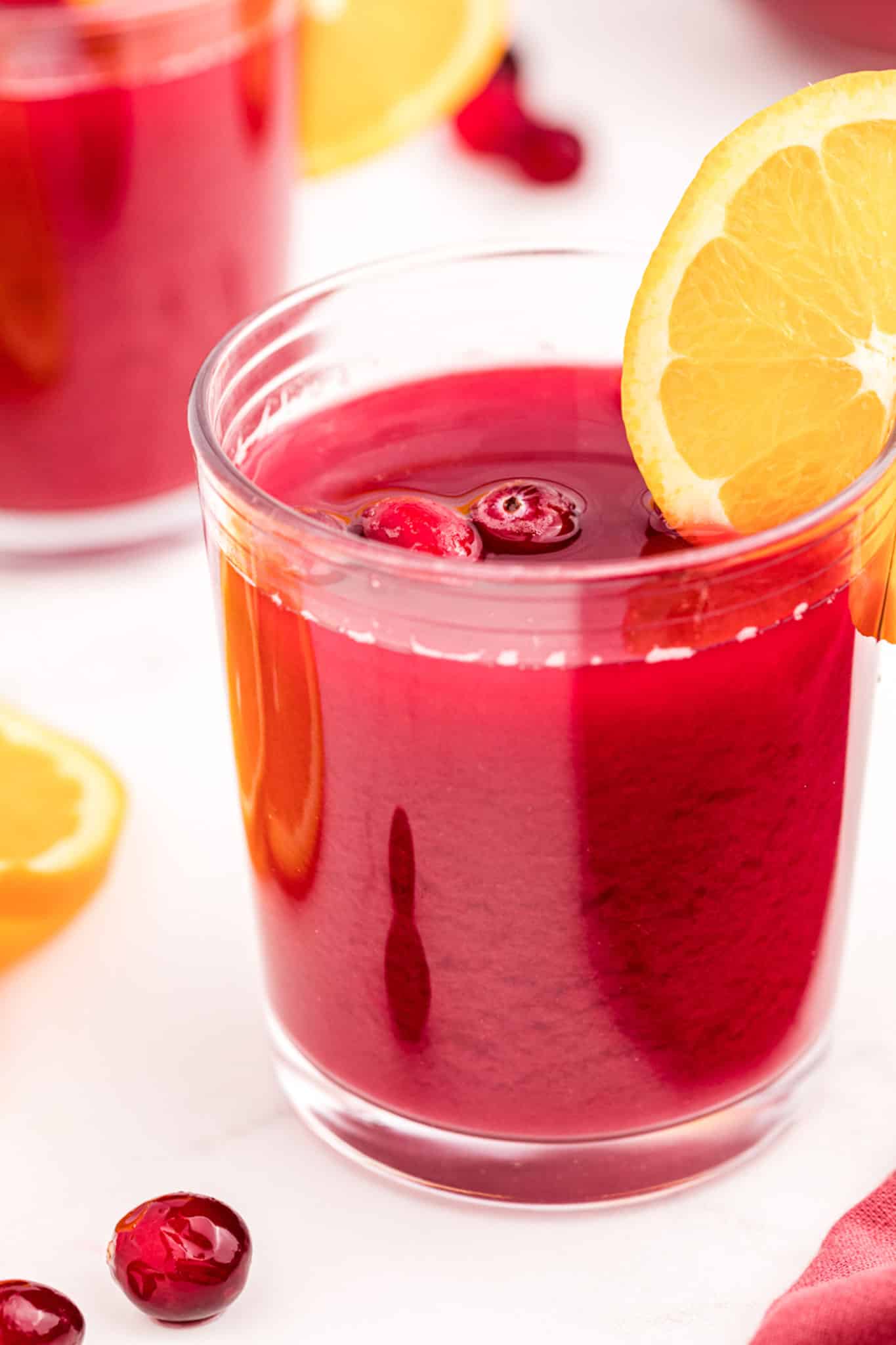 glass of red brunch punch garnished with an orange slice on a table.
