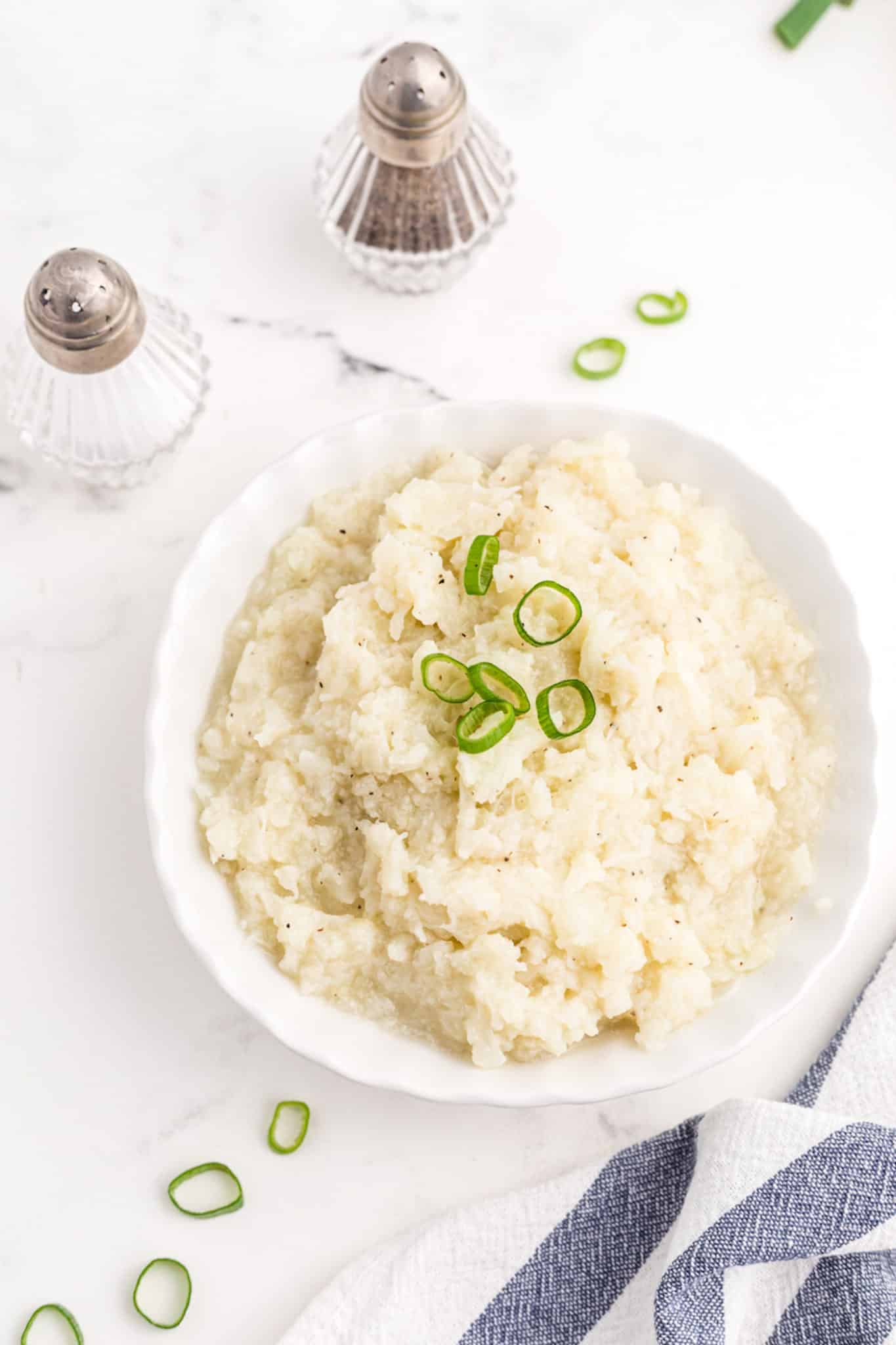 cauliflower mash in a white bowl with salt and pepper