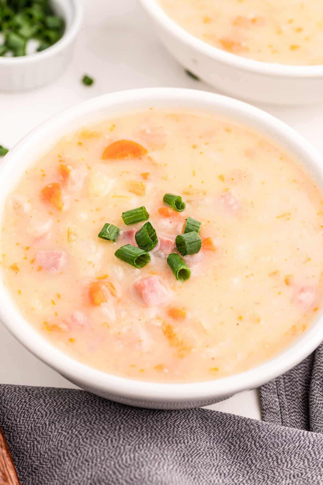 potato ham soup served in white bowl topped with green onions.