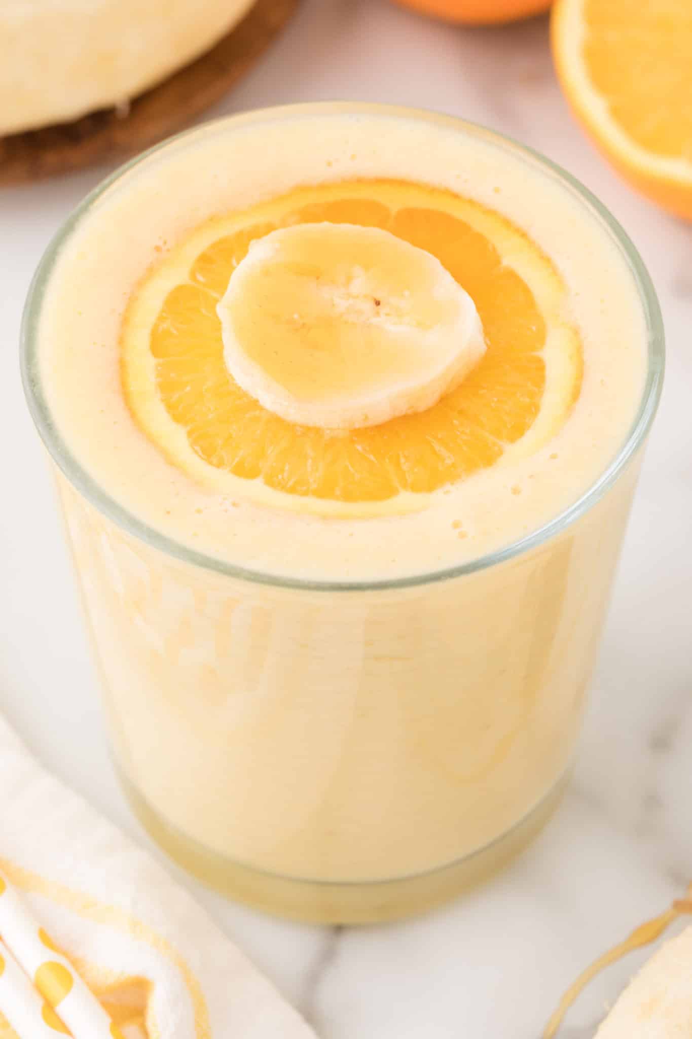 glass of orange smoothie with orange slice on top.