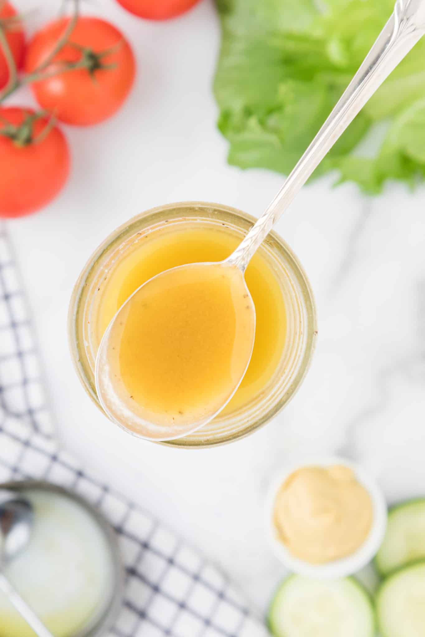 a spoonful of honey mustard on a table with tomatoes and lettuce.