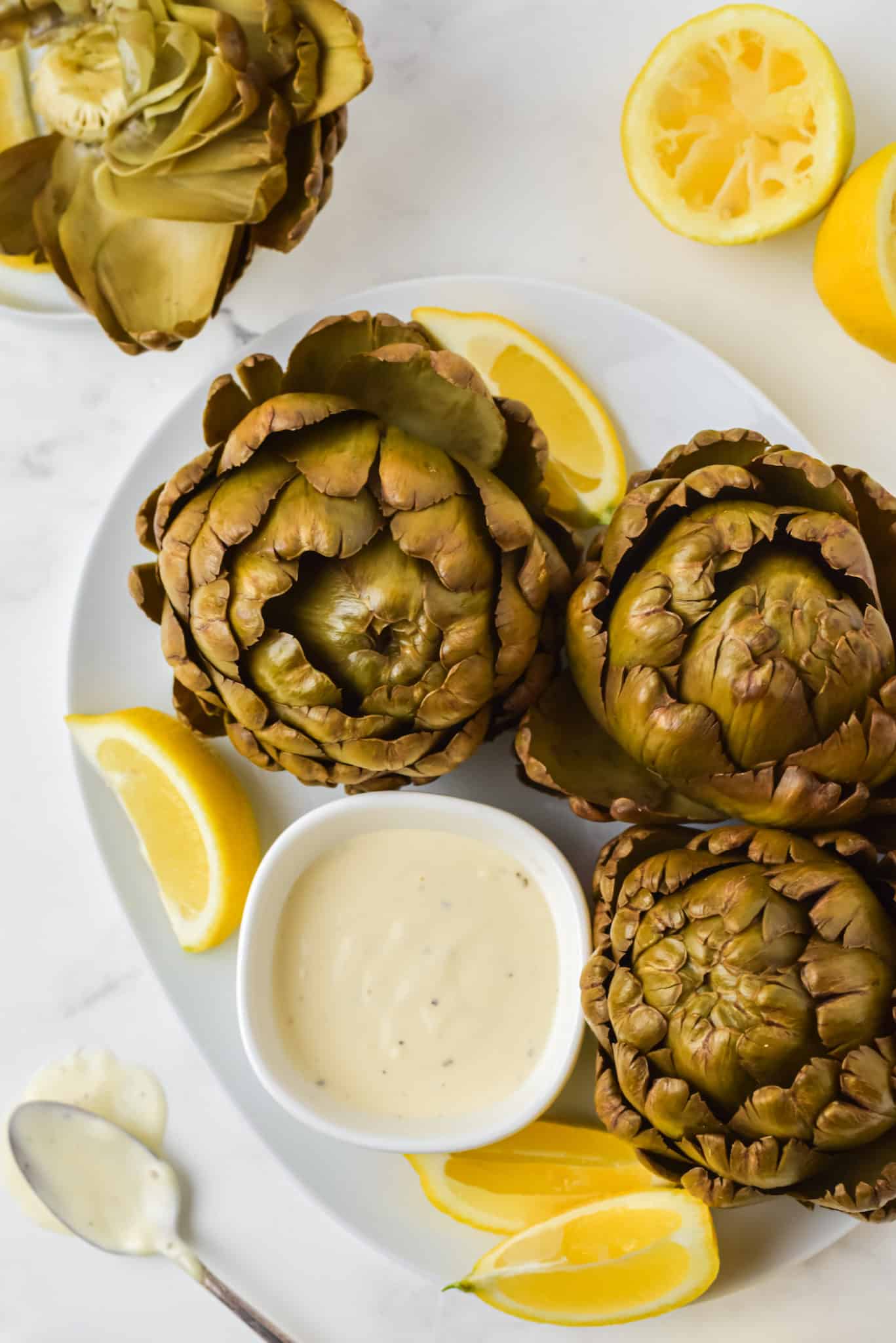 plate with cooked artichokes with lemon and dip sauce.