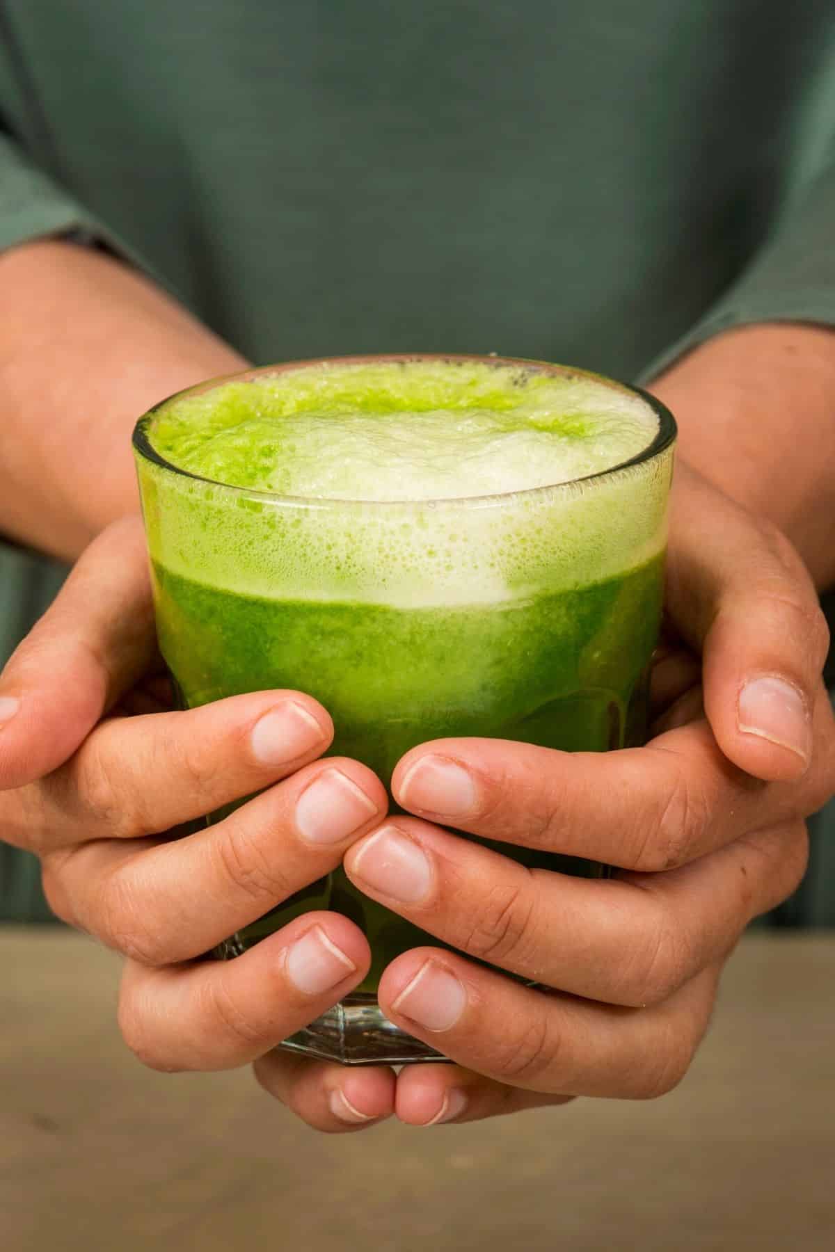 woman holding glass of green juice
