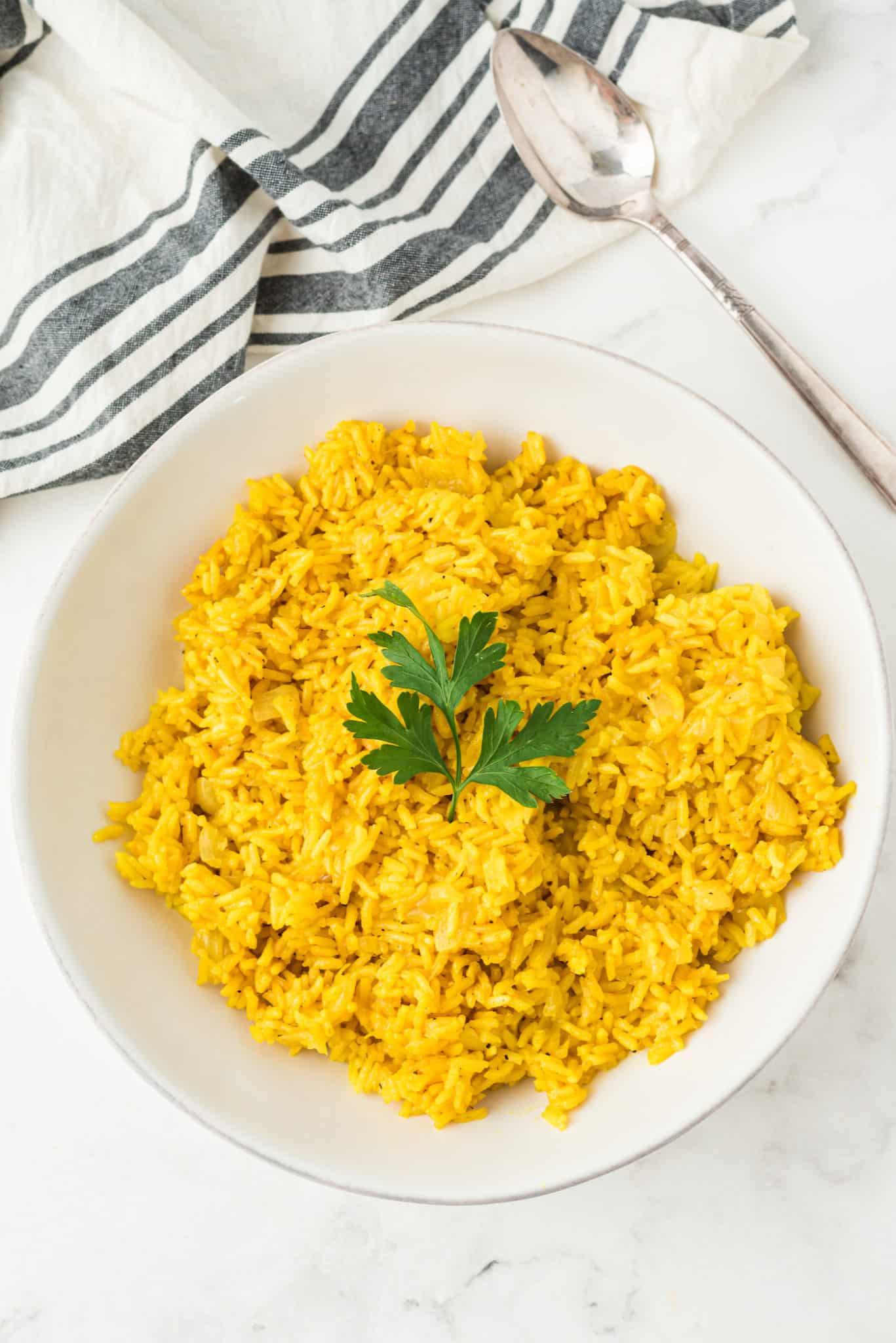 a bowl of instant pot yellow rice with a sprig of parsley on top.