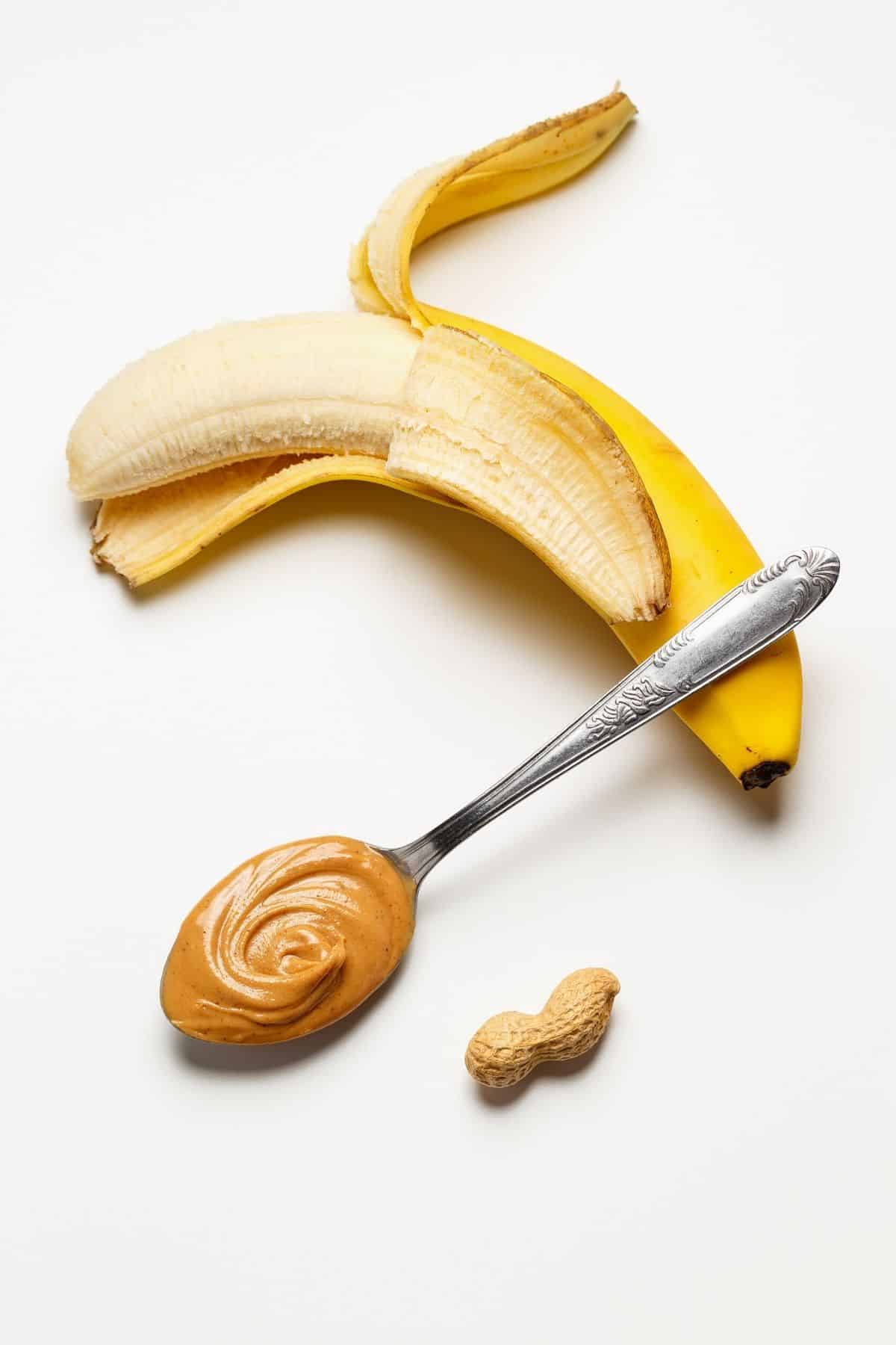 Banana with a spoon of peanut butter and a peanut.