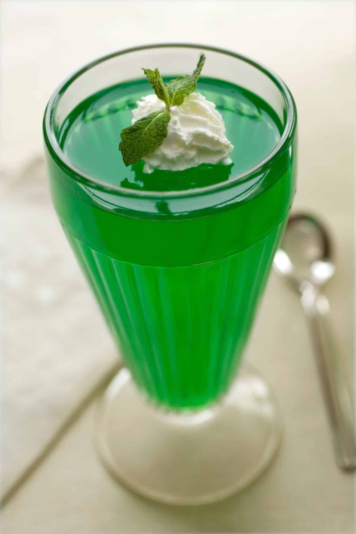 Green Jello in a cup with whip topping.