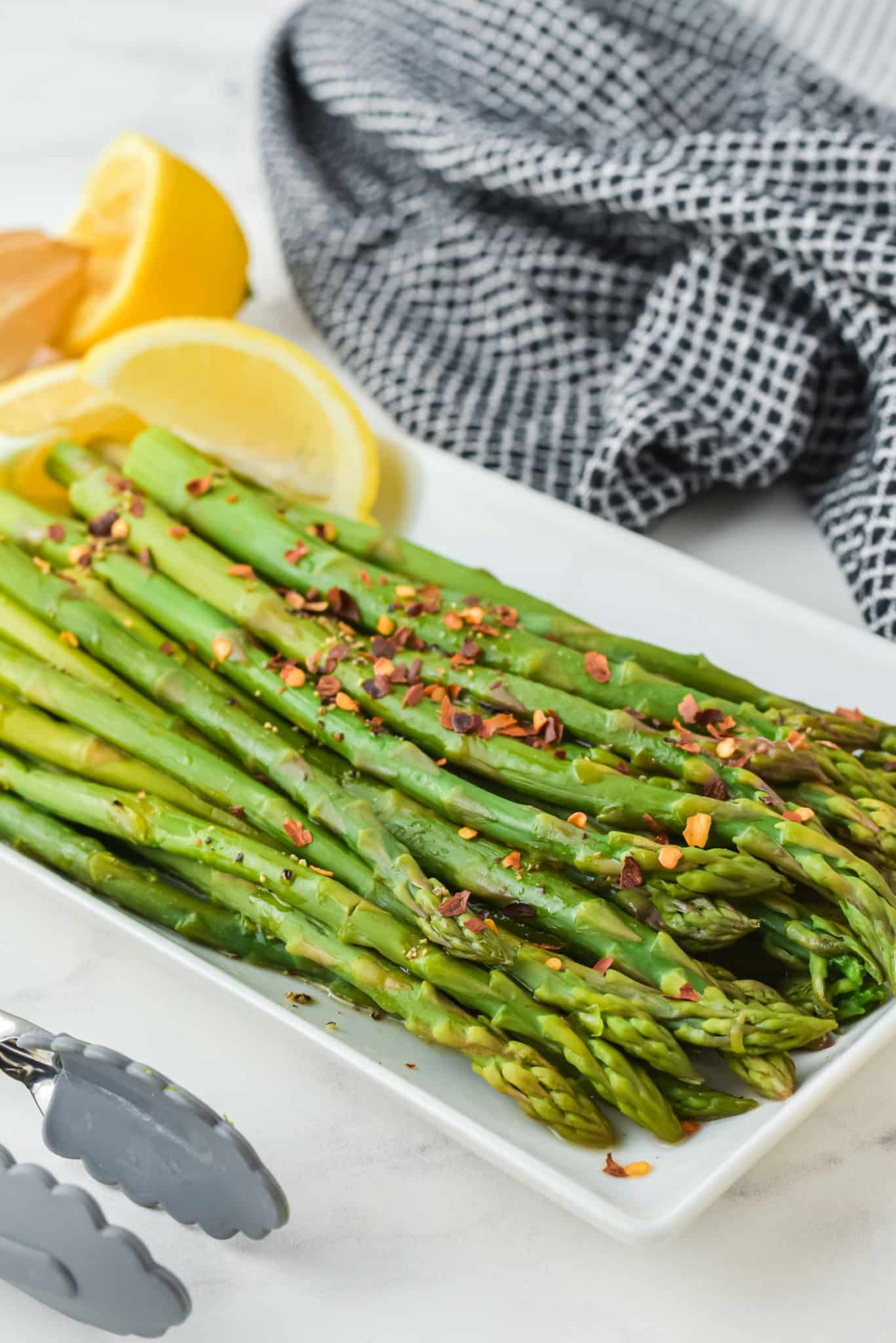 Red chili flakes sprinkled on asparagus spears on a white platter.