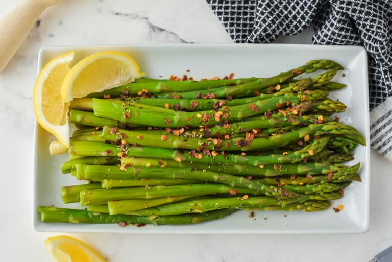 White rectangle platter of cooked asparagus with lemon wedges.