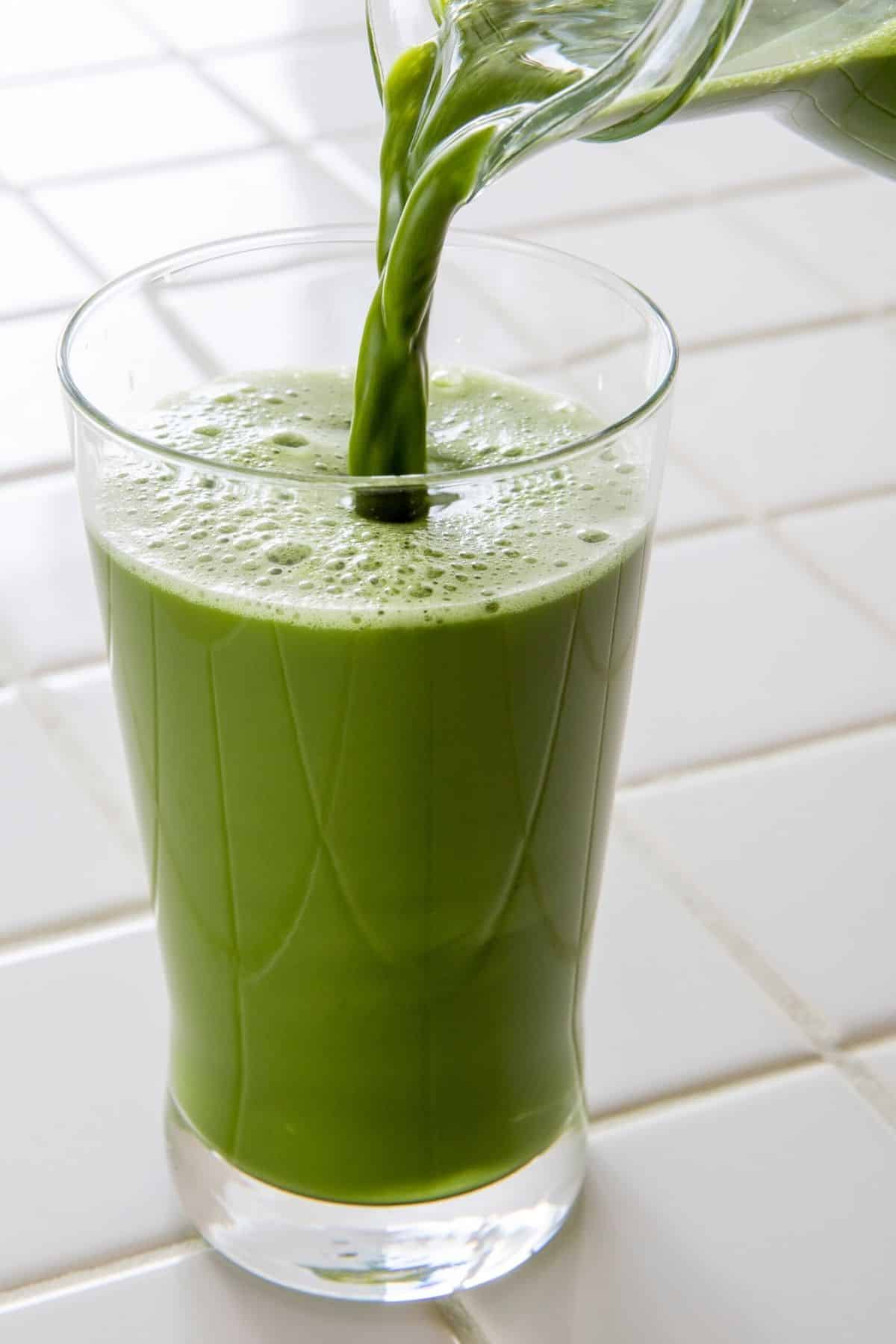 pouring detox vegetable green juice into glass.